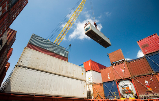 Refrigerated containers for Desmoines IA as seen from a bug's eye view. A crane lifts one up and holds it against the sky.
